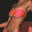 A model wearing a strapless, tie-back bandeau bikini top in magenta hue, with a vintage gold ring detail, posing in a seated position.