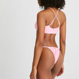 Model wears cheeky pink bikini bottoms with matching racer back bikini top